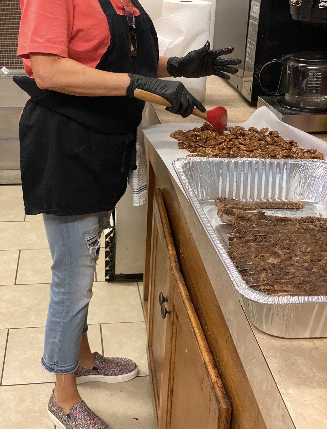 Tammie in an apron, seasoning a tray of food by hand in the kitchen